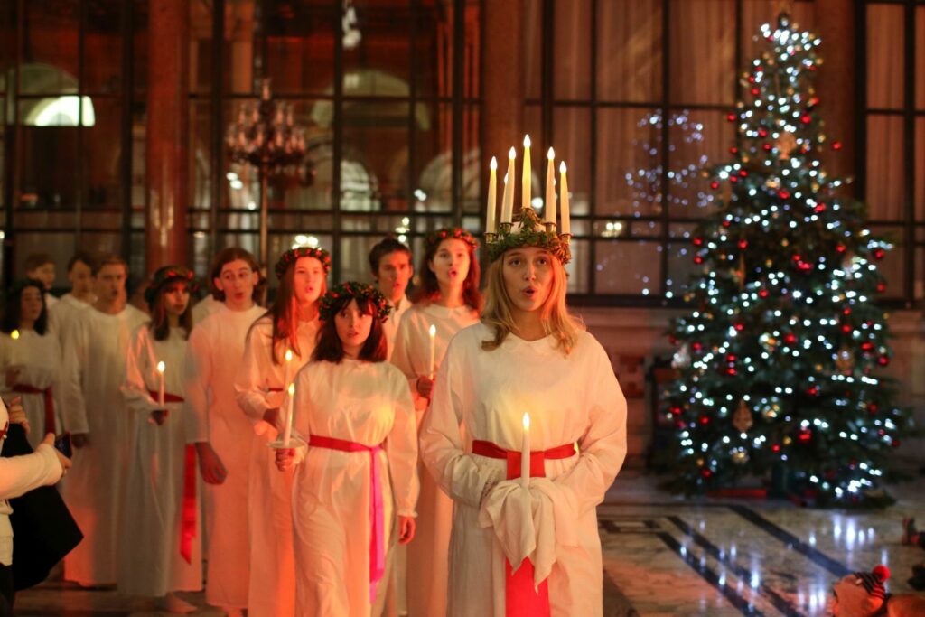 Procession de jeunes filles vêtues de blanc portant des bougies. La première porte une couronne de bougies allumées.