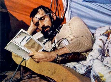 Homme sur un lit d'appoint lisant un livre et relié à différents instruments de mesure.